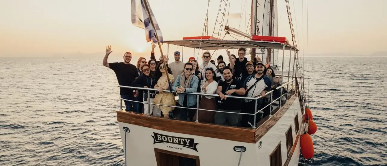 Gruppo numeroso di colleghi su un'imbarcazione a vela tradizionale durante un evento al tramonto