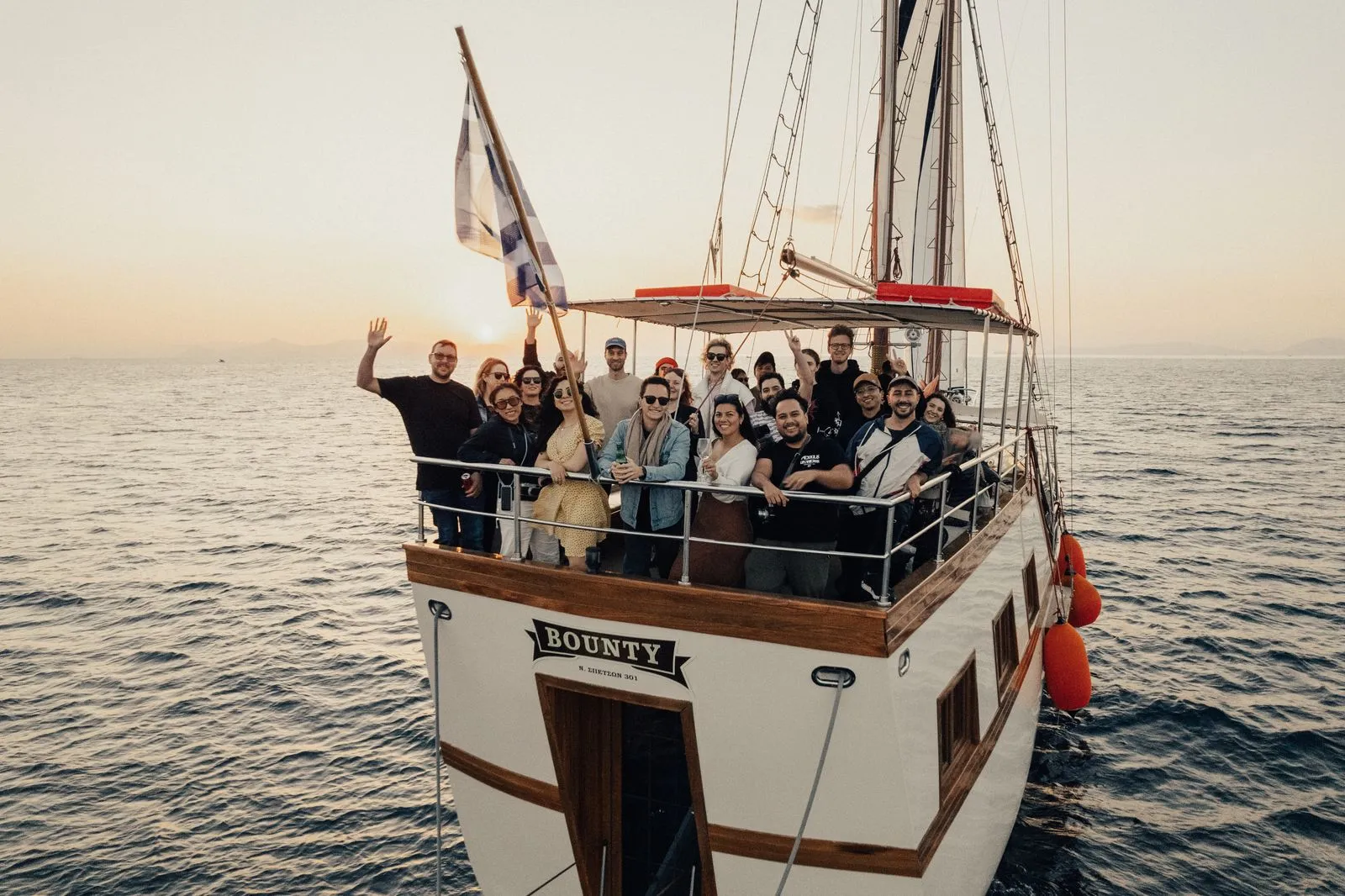 Gruppo numeroso di colleghi su un'imbarcazione a vela tradizionale durante un evento al tramonto