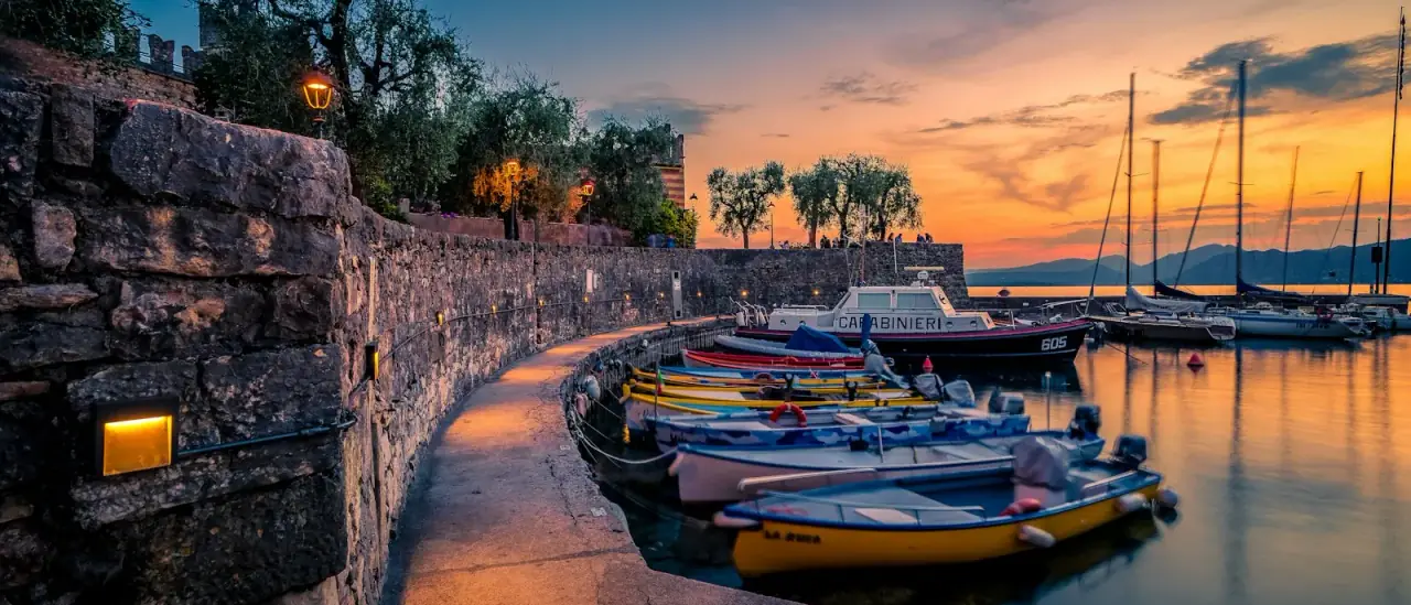 Barche colorate ormeggiate lungo il porto di Torri del Benaco al tramonto sul Lago di Garda